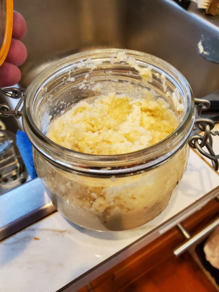 A glass jar, sitting on a white kitchen counter, is open to reveal the creamy paste of freshly prepared horseradish.